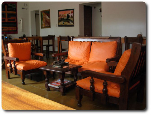 La foto muestra parte del salón para desayunos en la que se ven en primer plano cómodos sillones en un ambiente cálido y agradable donde está el resto de las mesas del salón cubierto del alojamiento